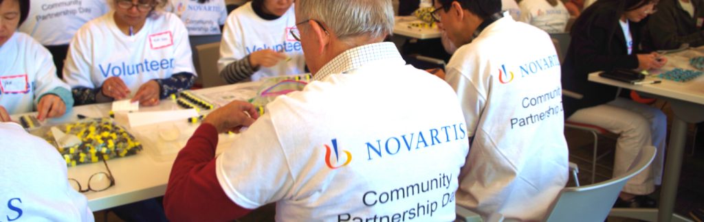 Novartis associates in matching commemorative t-shirts volunteer assembling STEM materials for high schools with PMD for Community Partnership Day 2019 in Cambridge, MA.